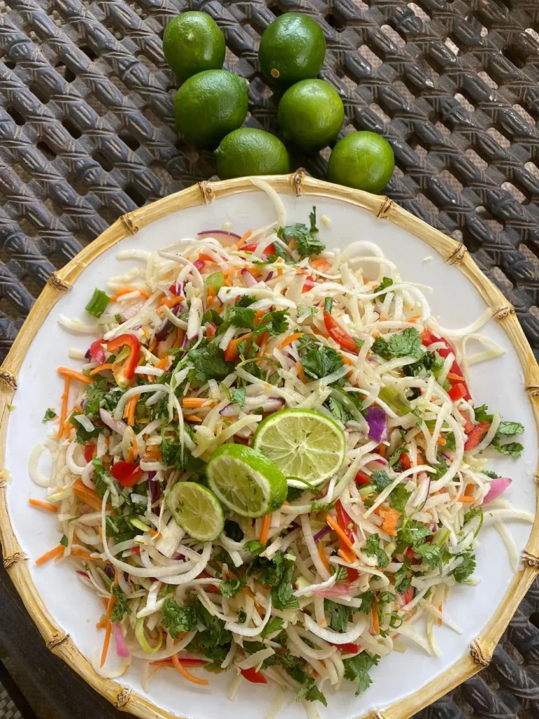 Colorful fresh vegetable slaw with lime, herbs, and mixed greens on a white plate